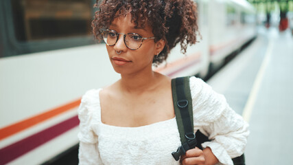 close-up portrait of a young woman in glasses with a backpack stands on the platform next to the train © Andrii Nekrasov