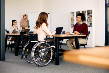Black businessman and his coworker with disability talk during meeting in office. - obrazy, fototapety, plakaty