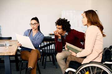 Group of colleagues talk while examining reports during business meeting in office.