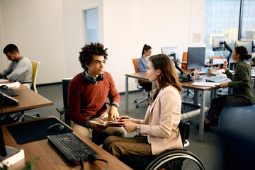 Black computer programmer and his colleague with disability cooperating while working at corporate...