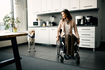 Happy businesswoman in wheelchair and her assistance dog at office kitchen. - obrazy, fototapety, plakaty