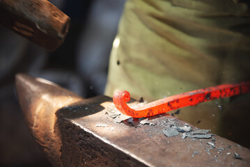Professional male blacksmith forming red hot metal on an anvil in interior blacksmith workshop.