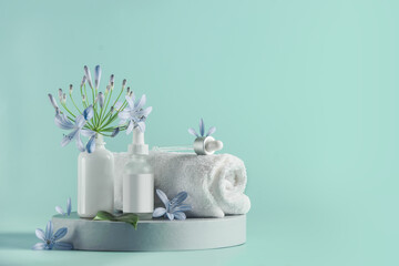 Beautiful wellness setting with white towel, pipette cosmetic bottles and blue flower on product podium at light turquoise background. Spa and beauty care concept. Front view with copy space
