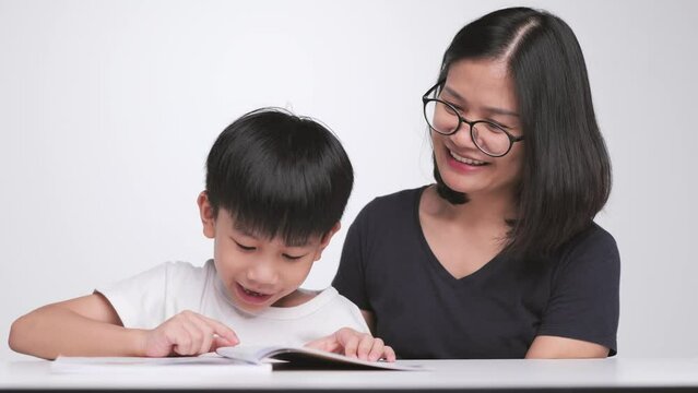 Asian mother teaches her son to read the book. A 6 year old boy learns how to spell the words.