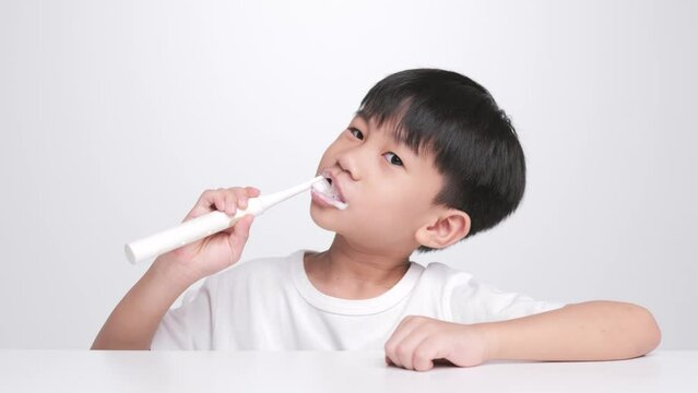 Asian kid brushing teeth with electric toothbrush. A 6 year old boy takes care of his bended baby tooth.