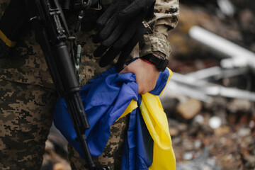 Naklejka premium Ukrainian military woman with the Ukrainian flag in her hands on the background of an exploded house