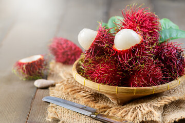 Fresh Rambutan fruits with leaves on bamboo basket on wood background.
