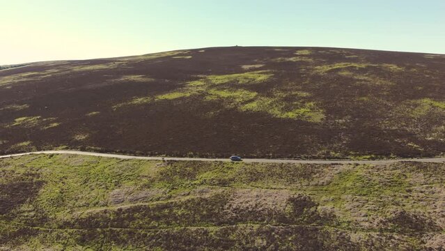 Aerial drone shot of car driving along scenic road through green countryside in Exmoor National Park, UK