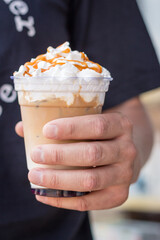 Man holding cold latte with whipped cream. Iced latte decorated with salt caramel topping in hand....