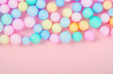 Foam beads of various colors brightly colored on pink pastel background with empty space.