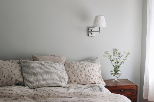 Bedroom View. Striped And Floral Linen Pillows, Blanket. Wooden Night Stand, Bedside Table Blooming Bishops Goutweed Flowers In Glass Vase. Mint, Sage Green Walll With White Lamp. Elegant Interior.