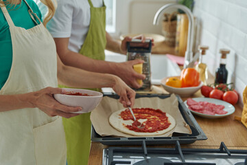 Close-up of couple making homemade pizza while standing at the kitchen together