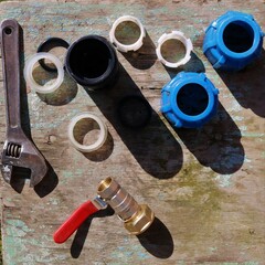 a set of parts for installing garden watering on an old peeling wooden surface top view in natural sunlight with harsh shadows from objects, plumbing accessories for household work
