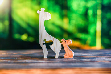 Wooden puzzle in the form of a family of handmade giraffes on the background of the forest.