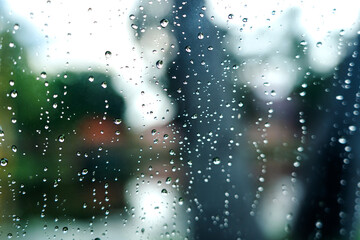 Raindrops on car windshield, blurred background of trees, inclement weather in rainy season.