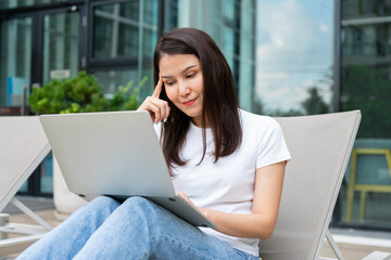 Happy young entrepreneur woman sitting on tanning bed beside pool and using laptop computer for remote online working digital, online business project in quiet yard of resort house, Work on vacation