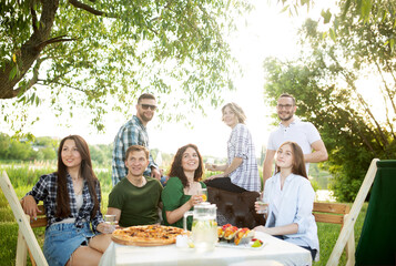 Group of young friends enjoying a picnic sitting outdoors fresh air spending weekend sunny day drinking beverage clinking cups, soft focus