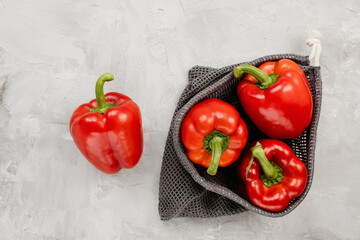 Fresh ripe sweet red bell pepper in eco-friendly reusable produce bag on gray background. Healthy grocery, vegan food and ingredients for cooking concept