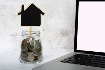 Wooden house model with jar of coins and notebook background. Copy sapce.
