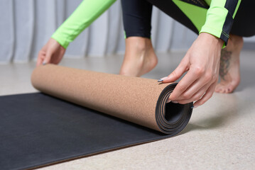 Image of a young woman in a gymnastics suit rolling up a mat after a workout. The concept of fitness, yoga, pilates.