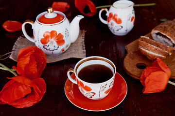 Traditional poppy seed bun with cup of tea and milk near poppies flowers and dishes with poppies ornaments. Delicious breakfast in summer. Lifestyle photography.