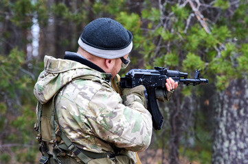 a man in camouflage shoots from a machine gun in the forest