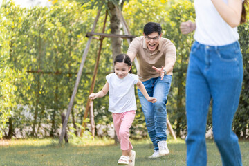 Fototapeta na wymiar Asian girl running on the lawn in a public garden Do activities together with your family in a fun and joyful way. There is a father and mother taking care of them closely.