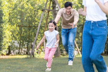 Naklejka na ściany i meble Asian girl running on the lawn in a public garden Do activities together with your family in a fun and joyful way. There is a father and mother taking care of them closely.