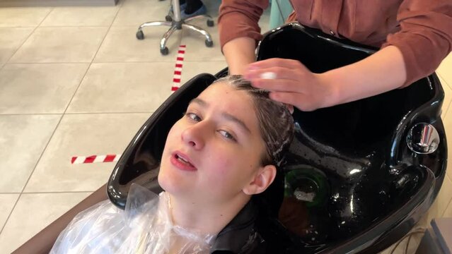 a girl - a hairdresser washes a girl of 13 years old head in a beauty salon, taking care of a shower in a beauty salon