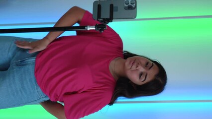 Funny Dancing teenage female blogger shoots video for stories, reels, social media on smartphone at home. Playful crazy teenager dance emotions. Magenta color t-shirt. Vertical shoot. 4k footage - Powered by Adobe