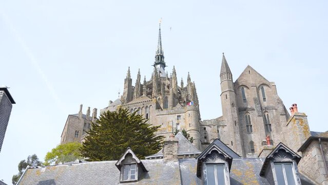 The roofs of the houses and the spiers of the church of the city of Mont Saint Michel against the sky at sunny noon. France. 4K video