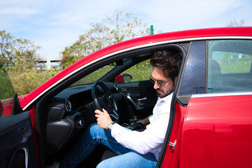 Young handsome man, sculpted body sitting in his red sports car. The man is wealthy and dressed in modern clothes. High standard of living and well positioned financially.