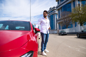 Handsome young man, sculpted body next to his red sports car. The man is wealthy and dressed in...
