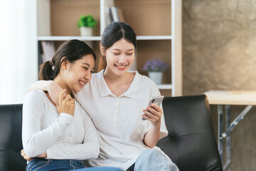 Two Happy young woman using their smartphones sitting on a sofa at home, pride day, lgbt concept.