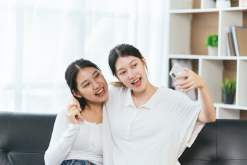 Two Happy young woman using their smartphones sitting on a sofa at home, pride day, lgbt concept.