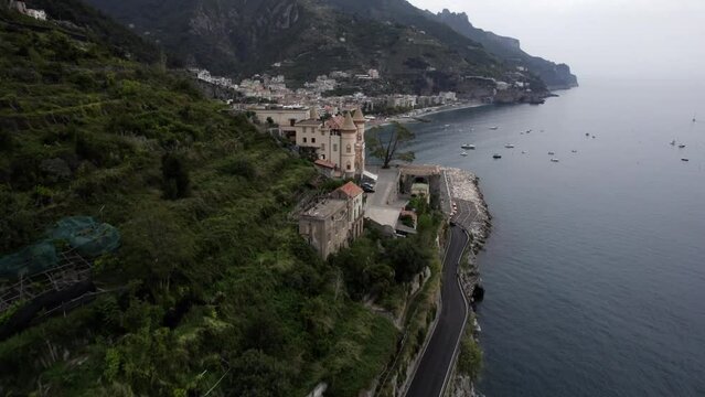 Drone video of a discovery plane passing a palace and revealing the city of Maiori on the Amalfi Coast, Italy. In the scene you can see boats, vehicles in traffic time.