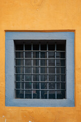 An old small window with a square lattice, like a prison on the yellow wall