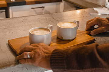 Old man's hands picking up wooden platter with two coffees