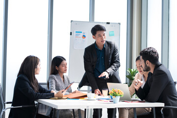An Asian businessman is presenting his company performance report to his boss or group of male and female colleagues with confidence and professionalism.