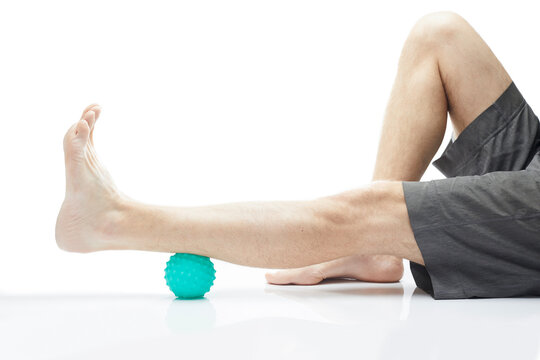 Close-up low section of man standing over massage ball against white background