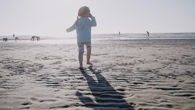 Little girl walking on an ocean beach on a sunny day. Chill and sunny day at the beach. Pastel colours shot of child running on the beach. High quality 4k footage