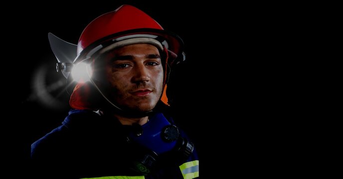 Caucasian firefighter wearing a helmet against spot of light and copy space on black background