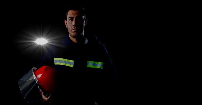 Caucasian firefighter holding a helmet against spot of light and copy space on black background