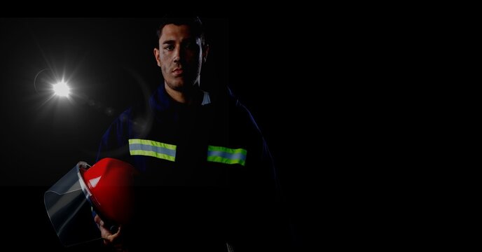 Caucasian firefighter holding a helmet against spot of light and copy space on black background