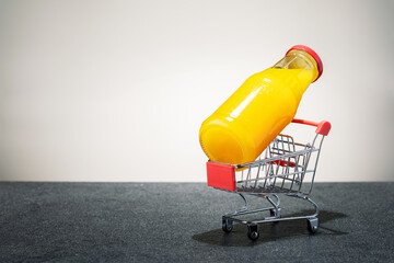 bottle with orange juice in shopping cart on tile surface with copy space. concept supply orange...