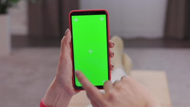 Close up view of female hands using smartphone with green mock-up screen. Scrolling through social media or online shop, swiping photos or pictures, surfing Internet,watching content videos blogs.