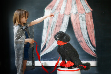 Cute child girl and black poodle dog playing circus. Tent drawn in chalk, dog training