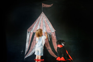 Cute child girl and black poodle dog playing circus. Tent drawn in chalk, dog training