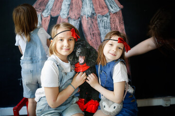 Fototapeta premium Children together with pet dog play in theater, circus. Black poodle and three European kids against background of black chalk board with circus pattern.