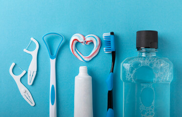 Toothbrush, tongue cleaner, floss, toothpaste tube and mouthwash on blue background with copy...